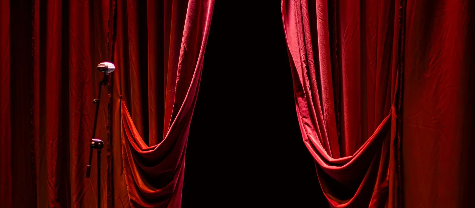 Microfono su un palco vuoto davanti al sipario rosso socchiuso